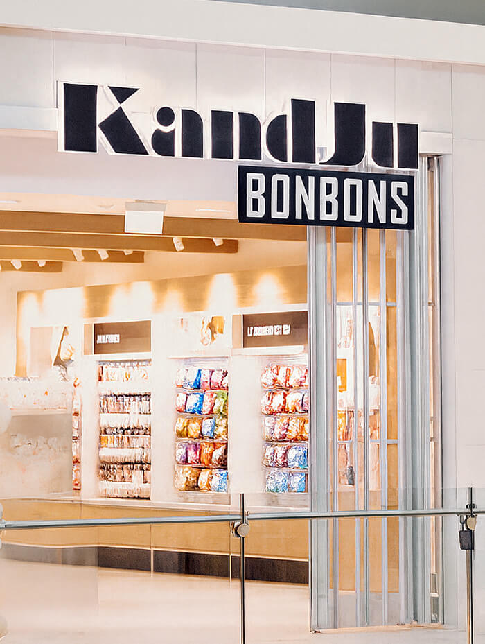 Entrée de la boutique KandJu Bonbons au Promenades St-Bruno, avec présentoirs colorés visibles à l’intérieur.